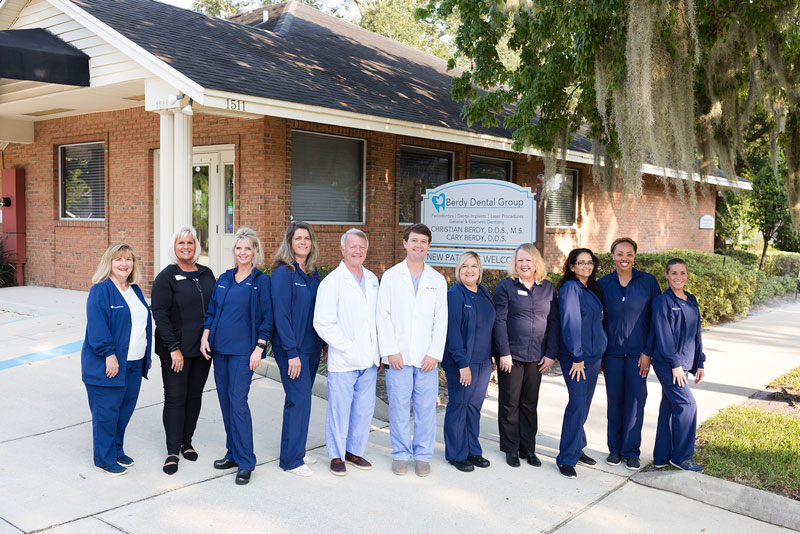 Dr. Christian Berdy and his son Dr. Cary Berdy in front of their dental office sign with their staff in Jacksonville, FL.